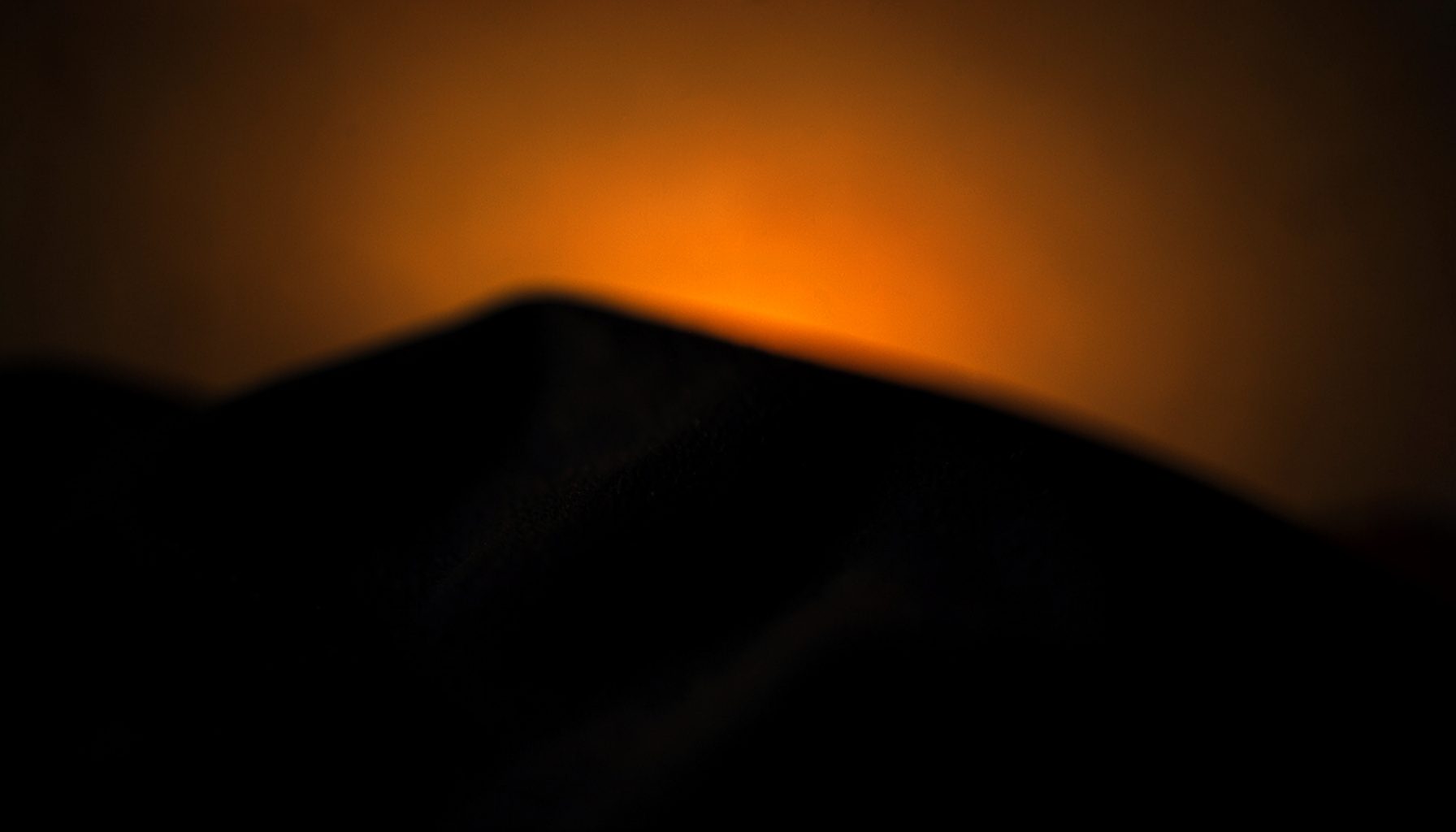 Dark moody photograph of soft black fabric draped in deep shadow against a warm amber gradient background