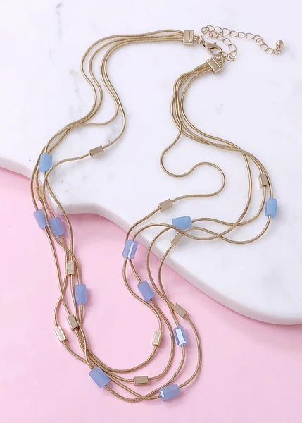 Layered gold chain necklace with light blue rectangular beads on white marble